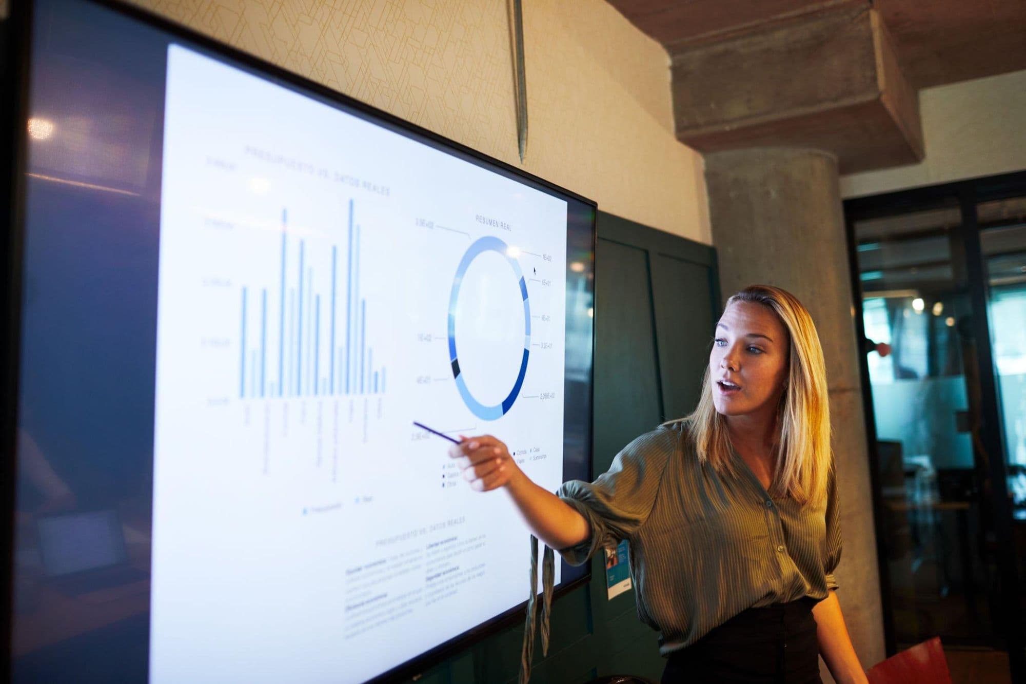 A consultant presenting performance data on a large screen to a team